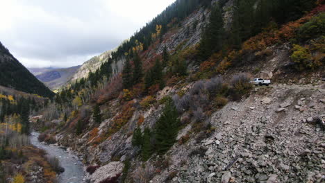 Cinematic-drone-aerial-4wd-truck-off-road-Marble-Crystal-Mill-stunning-autumn-Aspen-fall-colors-Southern-Colorado-Rocky-Mountains-peaks-Ouray-Telluride-camping-by-rocks-river-yellow-trees-forward