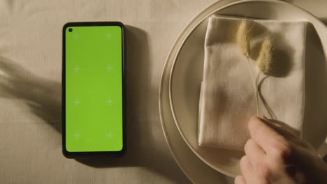 overhead of table setting with plate and green screen mobile phone