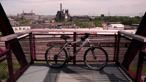 a bike sits dormant along the edge of a bridge with industry in the background