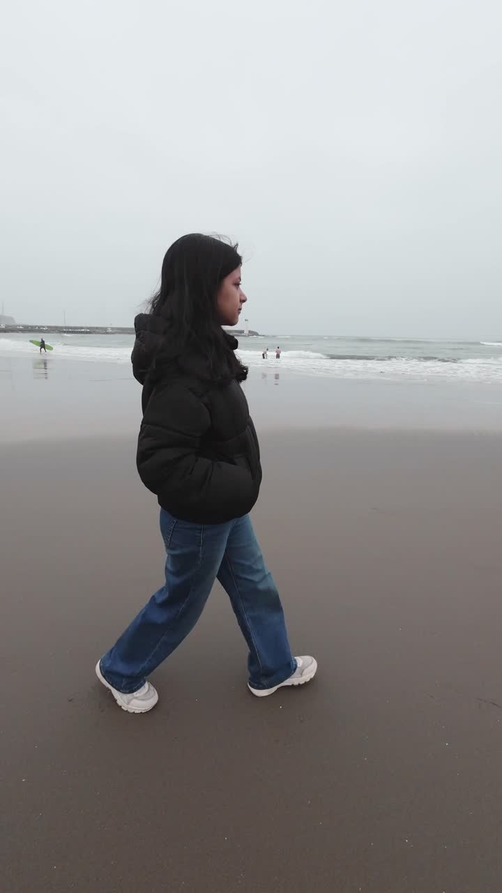Giovane donna che cammina lungo la spiaggia in una giornata nuvolosa