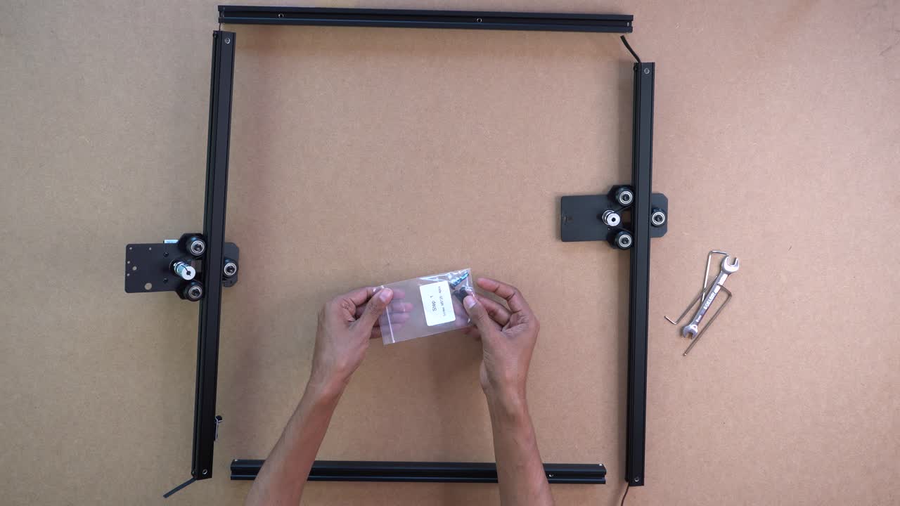 Hands assembling laser engraver frame on tabletop, parts and tools neatly laid out