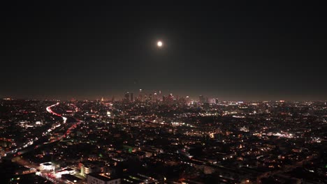 wide dolly aerial shot of the downtown skyline at night during the buck moon in los angeles, california. 4k