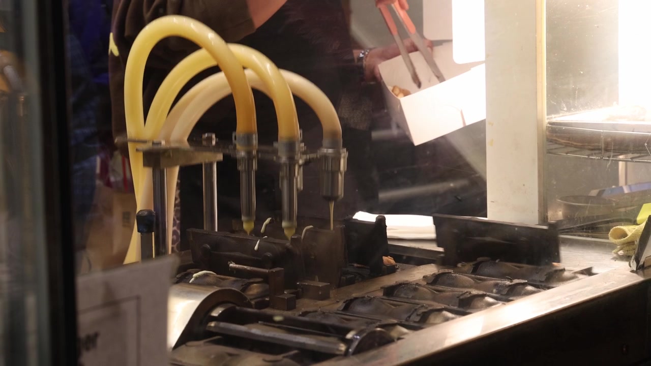 Machine making mini waffles on street food market, medium shot