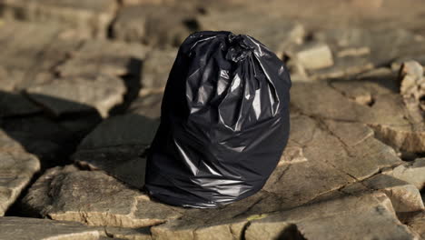 black trash bag lay on a rocky beach