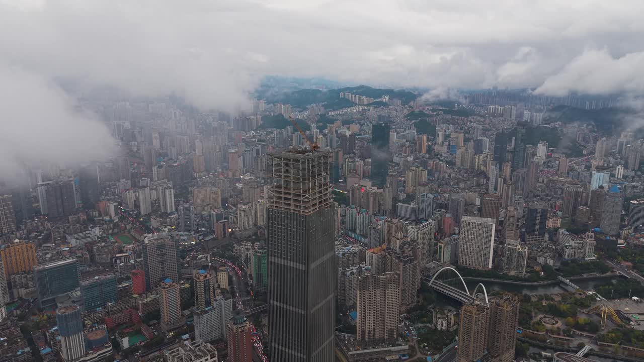 Aerial of the massive Hengfeng Guiyang Center Tower 1 under construction, soaring above the dense, sprawling cityscape of Guiyang, China. Urban growth and development