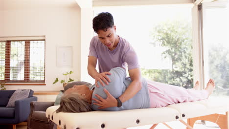 performing physical therapy, male physiotherapist assisting senior woman on massage table