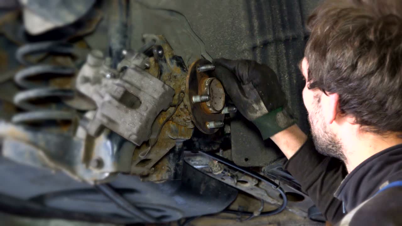 trabajador mecánico hombre moliendo pernos oxidados con herramienta de molienda eléctrica cerca de coche levantado