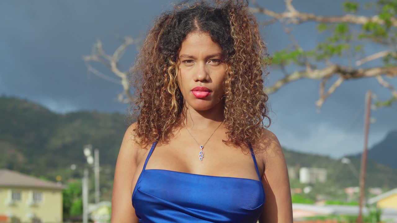 짧은 파란 드레스를 입은 곱슬머리 어린 소녀가 트리니다드의 열대 공원을 즐기고 있습니다.