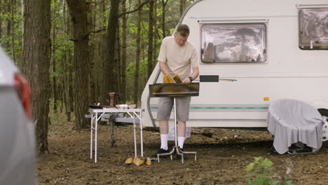 hombre recogiendo madera y poniéndola en una parrilla en el campamento en el bosque