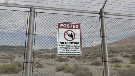 high quality 3d cgi render with a smooth dollying-out shot of a chainlink fence at a high security installation in a desert scene, with a no hunting no trespassing sign