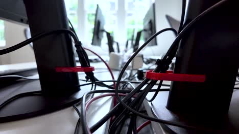 primer plano de la configuración del escritorio de la oficina con cables y cables organizados detrás de los monitores, destacando la gestión tecnológica del lugar de trabajo