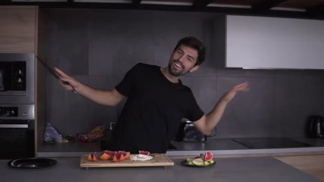 hombre gracioso cocinando desayuno vegetariano en la cocina en casa mientras baila y canta