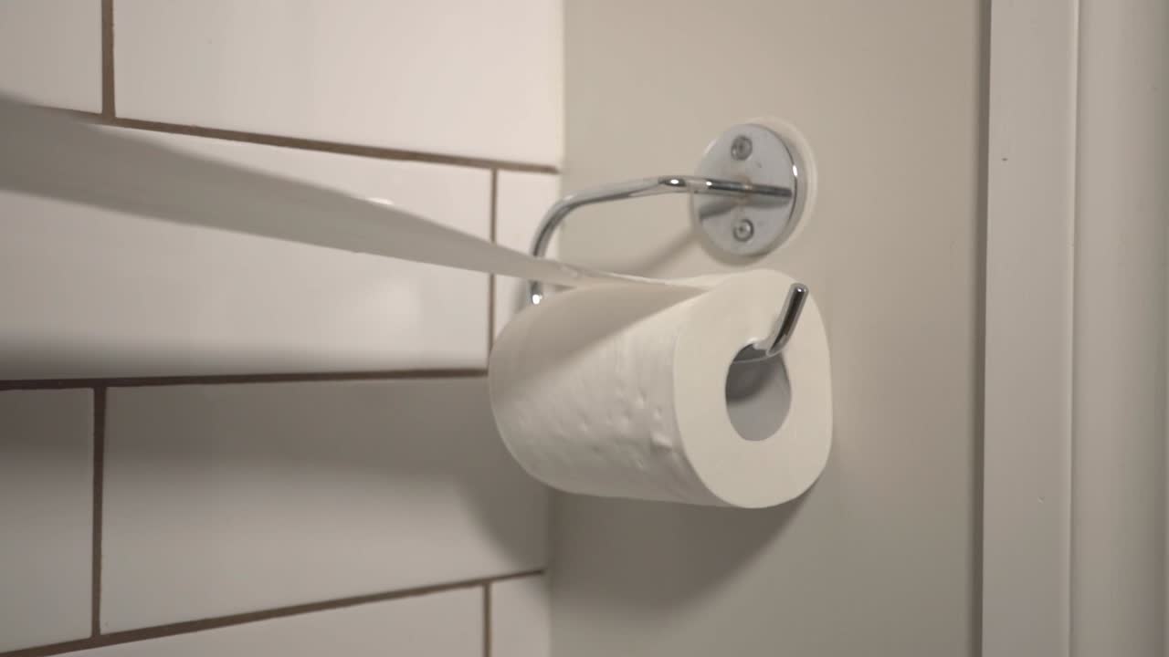 A Person Pulling A Long Pieces Toilet Paper On The Bathroom Wall - Closeup Shot
