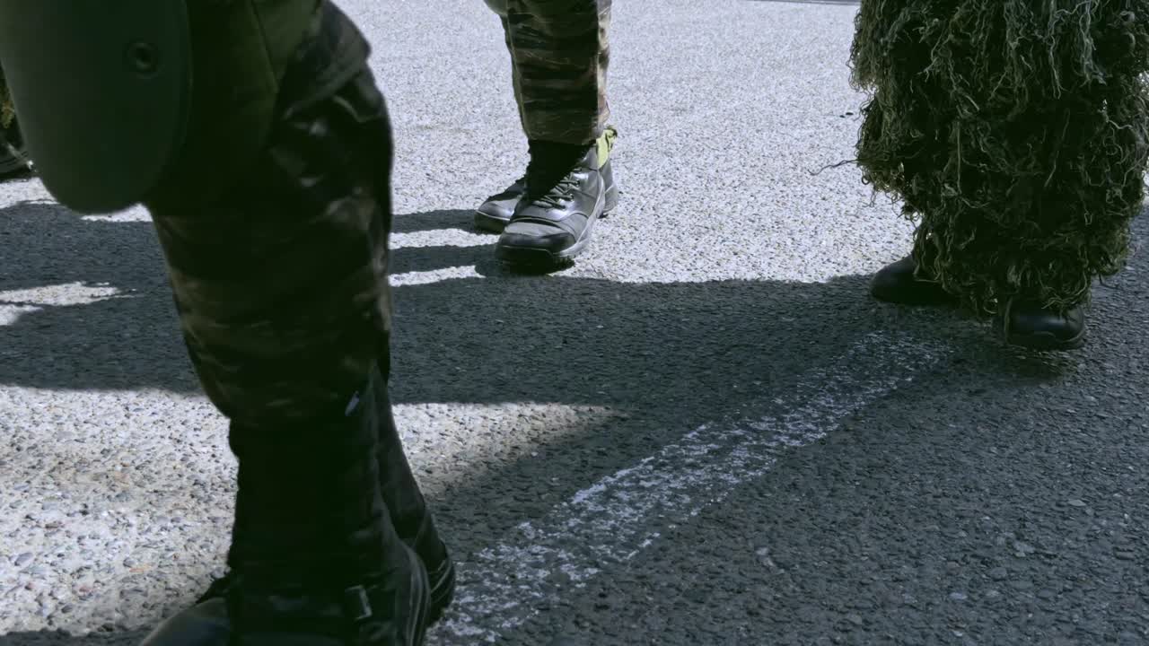 Low angle detail shot of army boots marching in sync on an asphalt road, representing military discipline and power