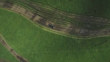 aerial view of a car driving on a dirt road through a grassy field.