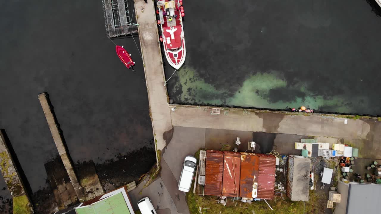 vista aérea de arriba hacia abajo del barco rojo y blanco tendido en aguas oscuras en un pequeño puerto en las islas feroe