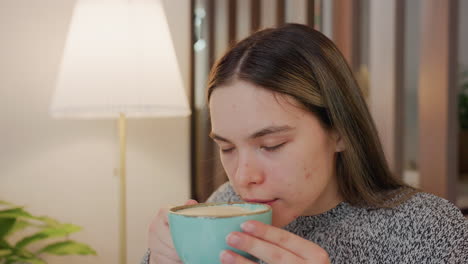 pretty lady savoring aroma from hot drink with calm satisfaction in cozy indoor space holding cup with both hands soft light from nearby lamp background features plant wooden decor peaceful ambiance