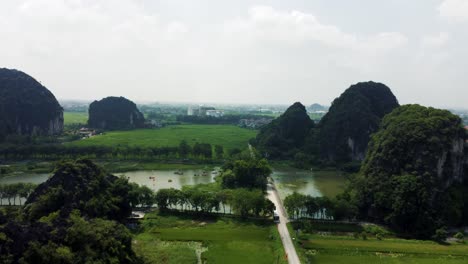 drone flying past a steep cliff revealing a river with little boat cruises in ninh binh, vietnam