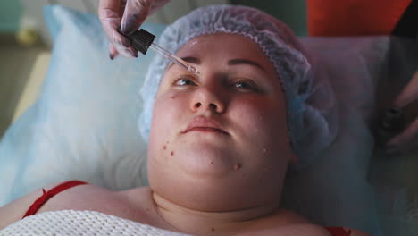 la esteticista aplica líquido de la pipeta en el rostro de la mujer