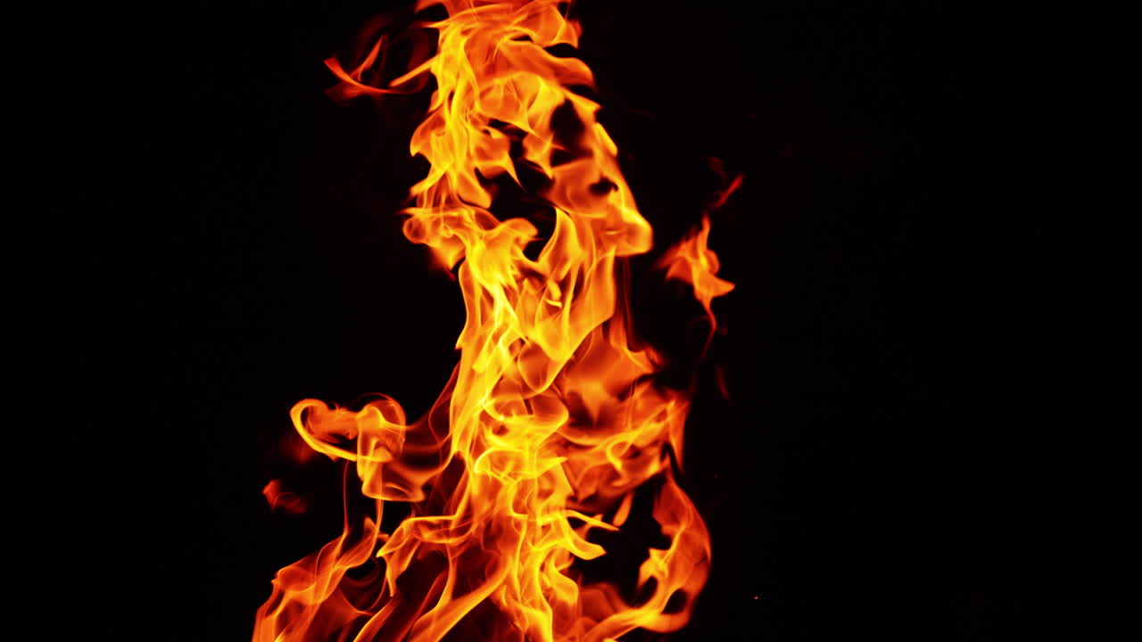 Beautiful fire flames moving in the darkness. Multiple sparks fly up and smoke rises behind. Close up.