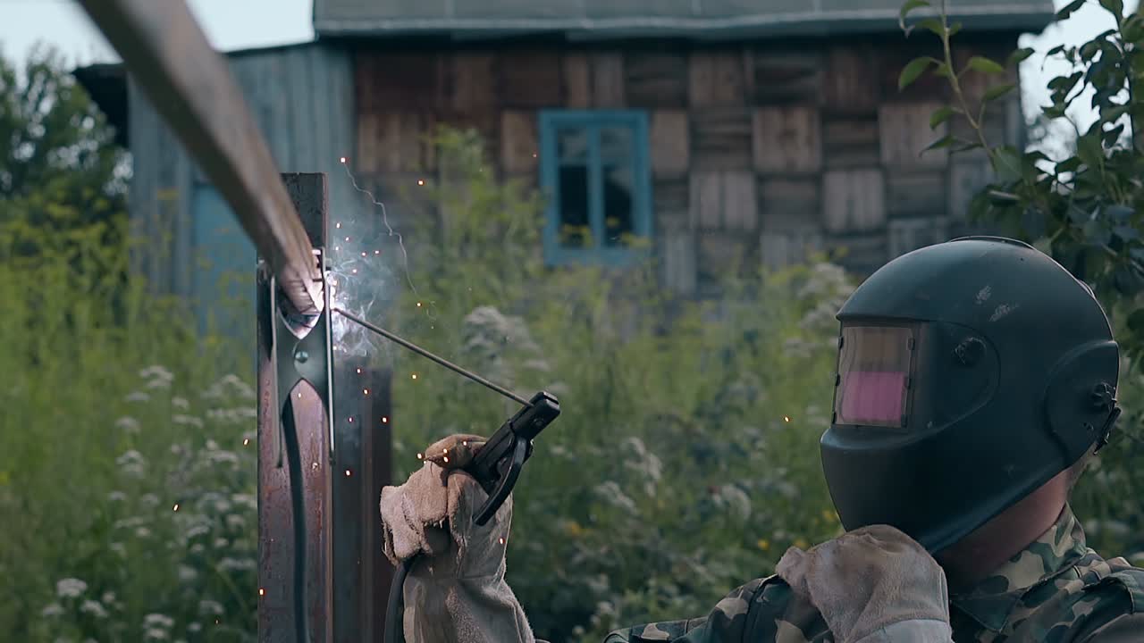 медленный человек сваривает забор и смотрит на законченную работу