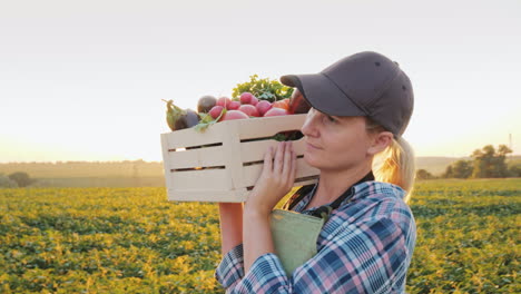 una agricultora con una caja de verduras frescas camina por su campo comiendo sano y vegeta fresca