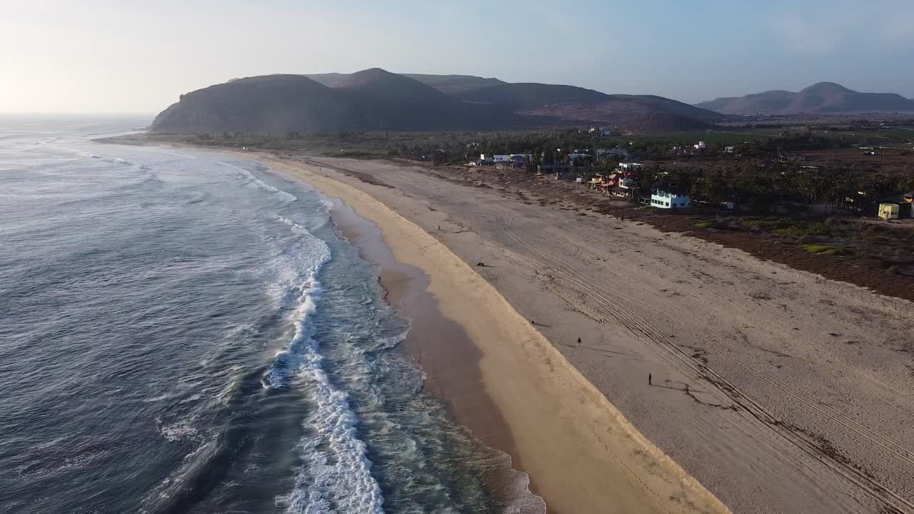 la gente camina por la playa al atardecer mientras las olas chocan contra la costa arenosa con montañas cerca de el pescadero