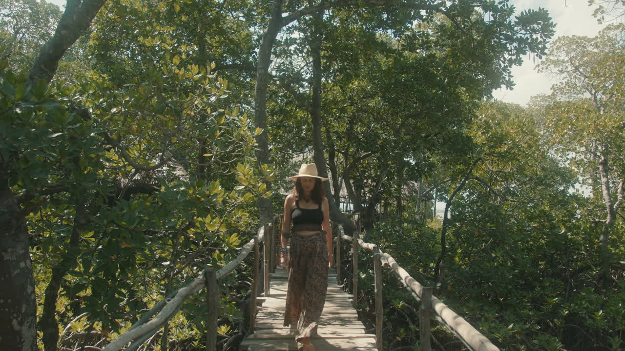 cámara lenta de una atractiva mujer caucásica con un sombrero de paja cruzando un puente de madera en un bosque verde