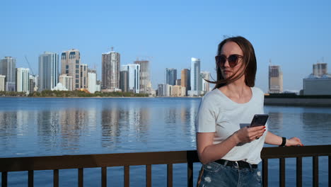 a girl with long hair dials a message on the smartphone at the quay of dubai