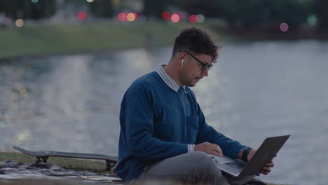 young man using laptop in city park by the river