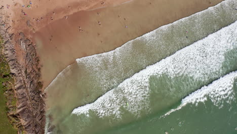 Birds-Eye-View-of-Waves-Crashing-Against-a-Golden-Sandy-Beach-in-Summer