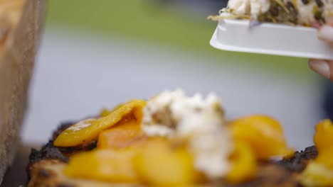 goats cheese being placed on some toast with yellow peppers