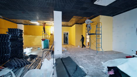 building team working inside the large unfinished premise. materials and equipment is in the middle of the room.