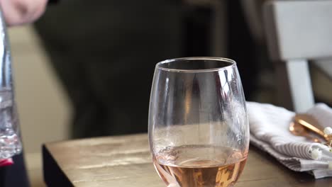 El-Servidor-Recoge-Rápidamente-Una-Copa-De-Vino-Rosado-En-Una-Copa-De-Vino-Sin-Tallo-Después-De-Terminar-De-Verter-De-La-Botella-De-Vino,-Cierra-La-Mano-Con-Esmalte-De-Uñas-Rosa-Y-Servilleta-En-El-Fondo,-Color-Blanco-Y-Rojo-Dorado