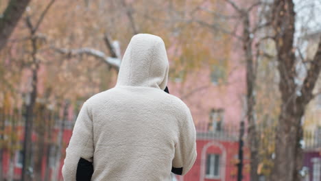 vista trasera de una persona con chaqueta de invierno caminando y hablando por teléfono con un fondo borroso con árboles secos y edificios, evocando una escena de invierno pacífica en un entorno urbano