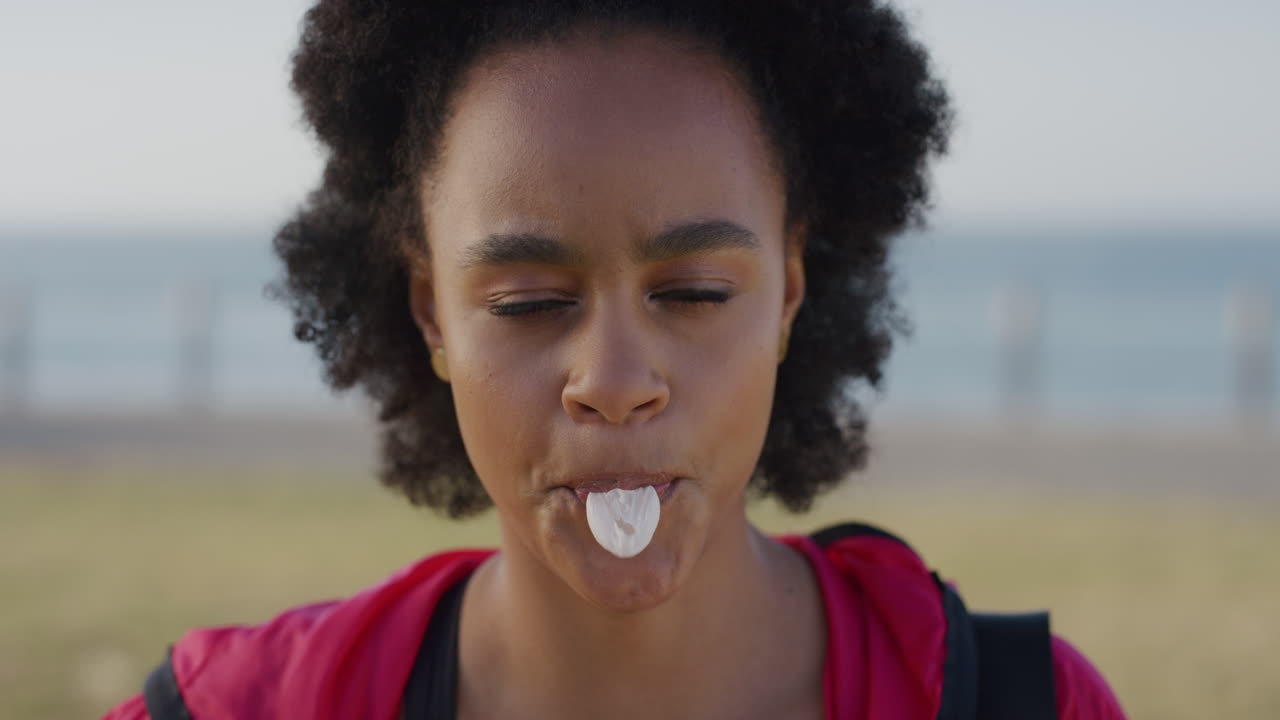 portrait joven afroamericana animada soplando burbuja de chicle disfrutando de diversión lúdica riendo chica negra feliz en vacaciones en el fondo de la playa