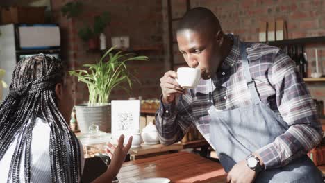 smiling african american female and male coffee shop owners talking and drinking coffee, slow motion