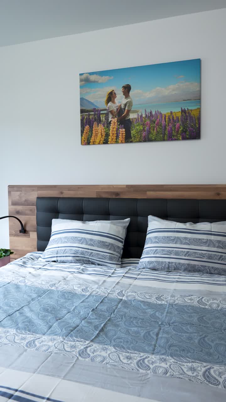 Dormitorio moderno y ordenado con cama hecha, almohadas y arte de pared con fotos de pareja, vista vertical de un estilo de vida limpio y ordenado