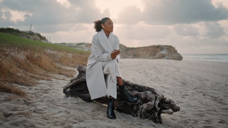 mujer elegante hablar auriculares en la playa de otoño. tranquila chica de cabello negro descanso océano