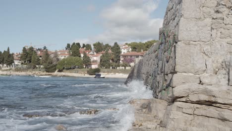 Slow-motion-side-shot-of-water-crashing-against-rocky-wall-and-city-in-background