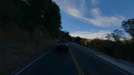 fpv drone view of black car driving fast on road at evening