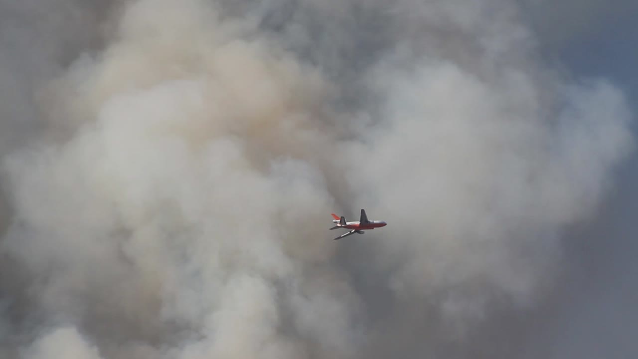 Gran avión volando a través del humo combatiendo un incendio forestal en California