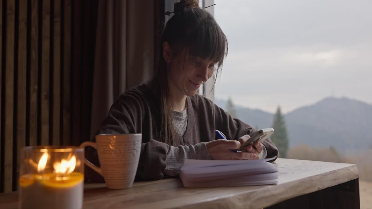 Woman using phone at a table with a candle and mountain view