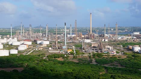 cloud shadow passes over lush green landscape to reveal oil refinery flare stacks in distance