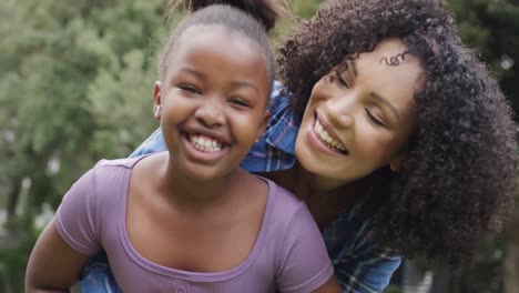 portrait of happy african american mother and daughter embracing and smiling in garden, slow motion