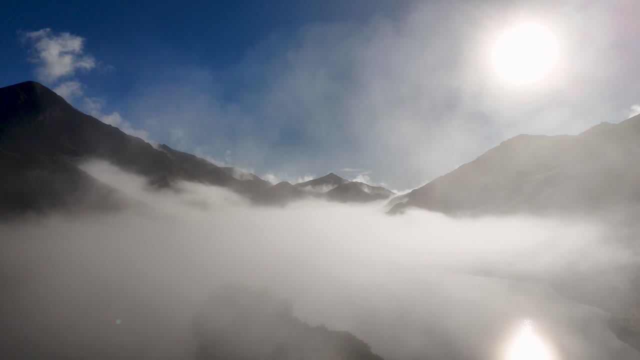 Drone captures misty mountains in Queenstown, New Zealand, during a serene winter sunrise with clear blue skies