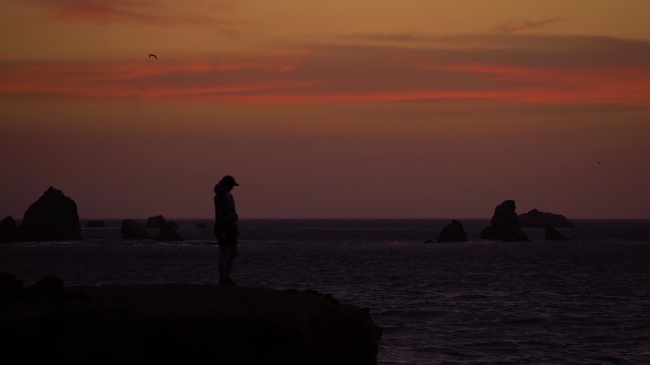 Silhouette person on coastal cliff during dramatic sunset, dark scene, slowmo HD