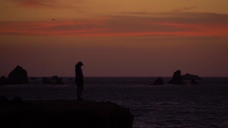 silhouette person on coastal cliff during dramatic sunset, dark scene, slowmo hd