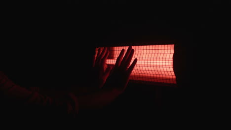 hands warming near a red electric heater at night