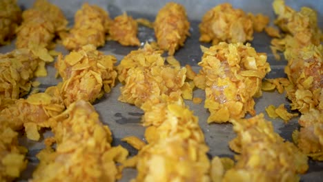 pollo crudo cubierto de copos de maíz en una bandeja para hornear